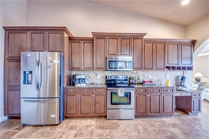 Kitchen featuring arched walkways, decorative backsplash, stone countertops, and stainless steel appliances