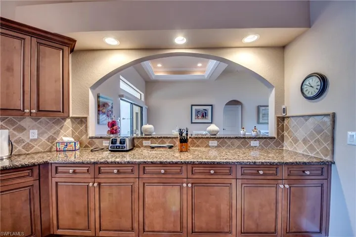 Kitchen featuring a tray ceiling, arched walkways, backsplash, and light stone countertops