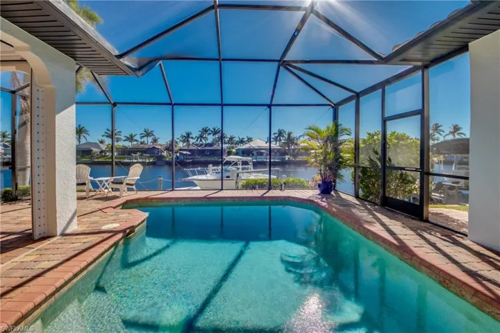 Pool featuring glass enclosure, a patio area, and a water view