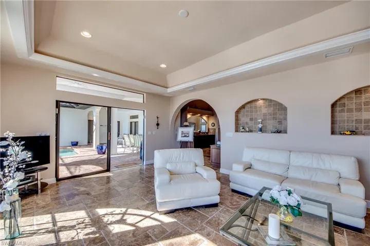 Living room featuring stone tile floors, baseboards, visible vents, arched walkways, and a raised ceiling
