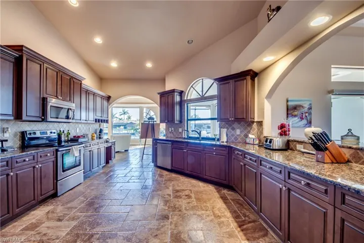 Kitchen featuring tasteful backsplash, stone tile floors, stone counters, appliances with stainless steel finishes, and arched walkways