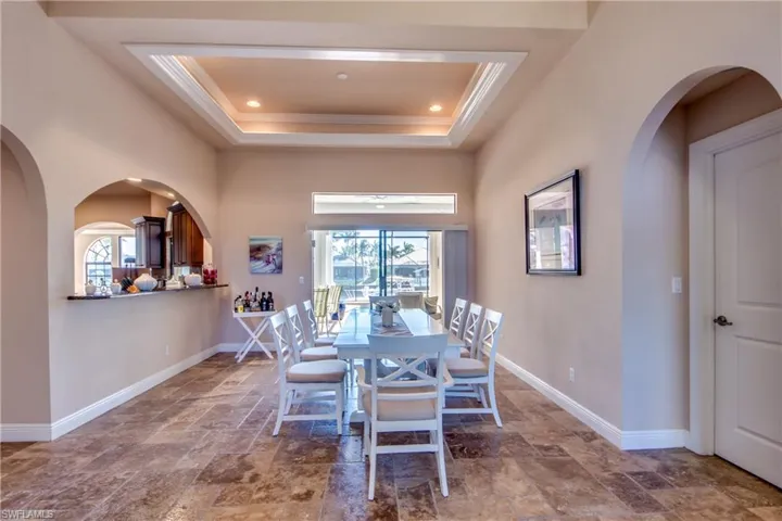 Dining space with baseboards, a tray ceiling, recessed lighting, stone finish floor, and crown molding