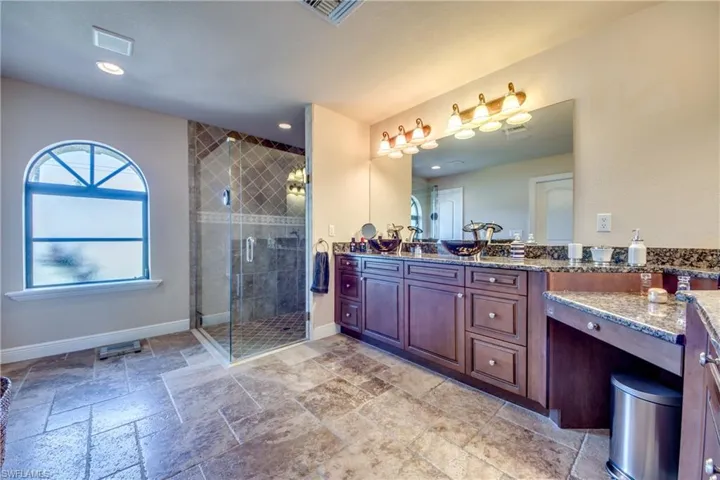 Full bath featuring visible vents, stone tile flooring, a shower stall, baseboards, and vanity