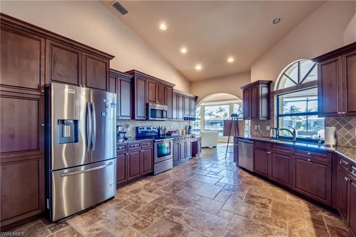 Kitchen featuring stone tile floors, visible vents, dark stone counters, arched walkways, and appliances with stainless steel finishes