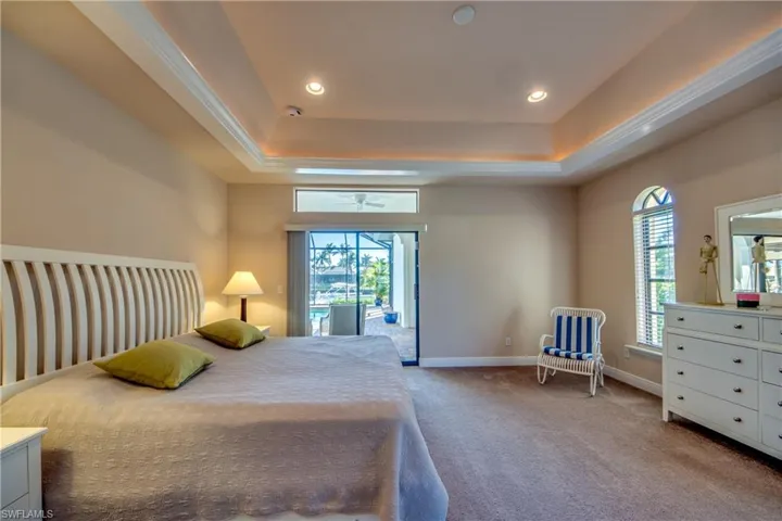 Bedroom with a raised ceiling, recessed lighting, light colored carpet, and baseboards