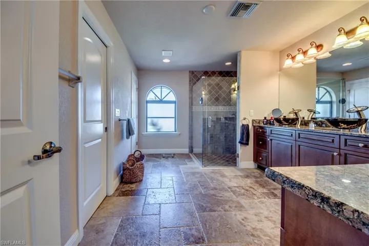 Bathroom featuring vanity, stone tile floors, baseboards, visible vents, and a stall shower
