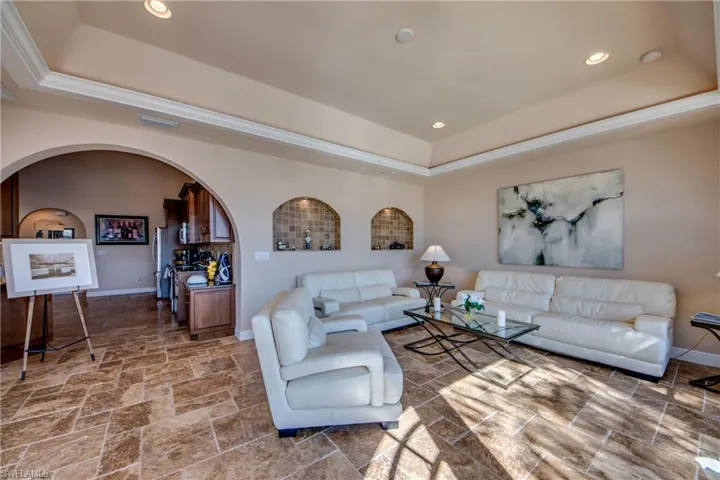 Living area featuring baseboards, visible vents, arched walkways, stone finish flooring, and a raised ceiling