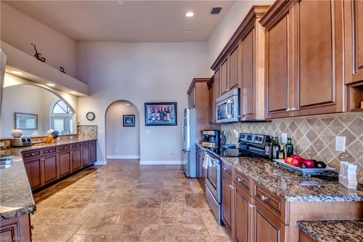 Kitchen with brown cabinetry, baseboards, visible vents, arched walkways, and stainless steel appliances