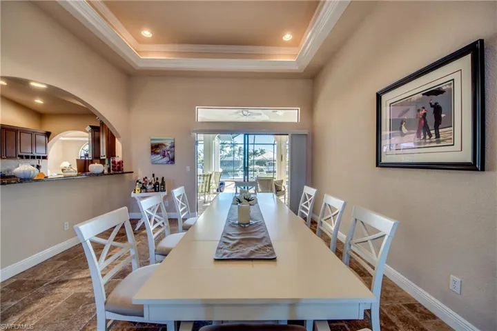 Dining space featuring arched walkways, a raised ceiling, crown molding, and baseboards