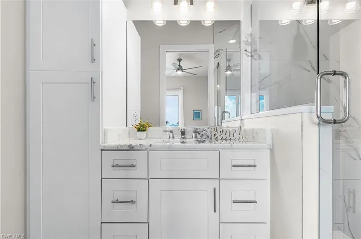 White shaker-style cabinetry with brushed nickel hardware, a single vanity with a white countertop, an undermount sink with a chrome faucet, and a large mirror with overhead lighting - Virtually Edited Image