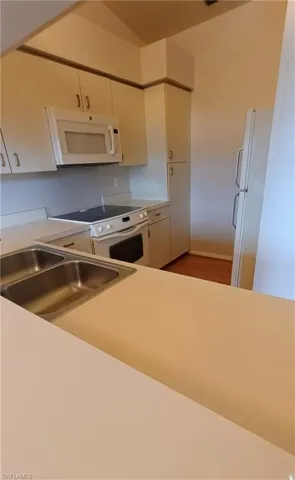 Kitchen with white appliances, white cabinetry, light countertops, and wood finished floors