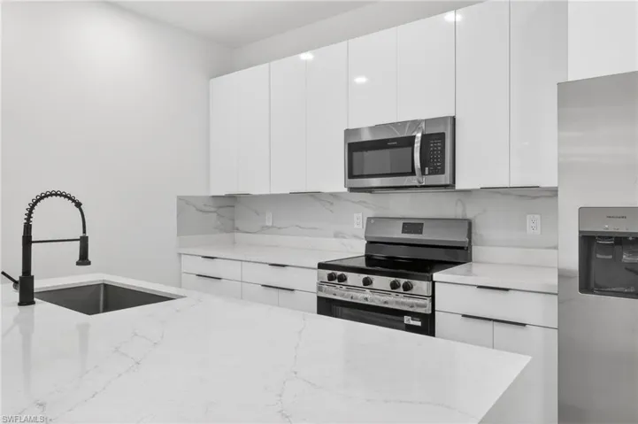 Modern kitchen featuring white cabinetry, quartz countertops, a stainless steel appliance suite, and a matte black gooseneck faucet