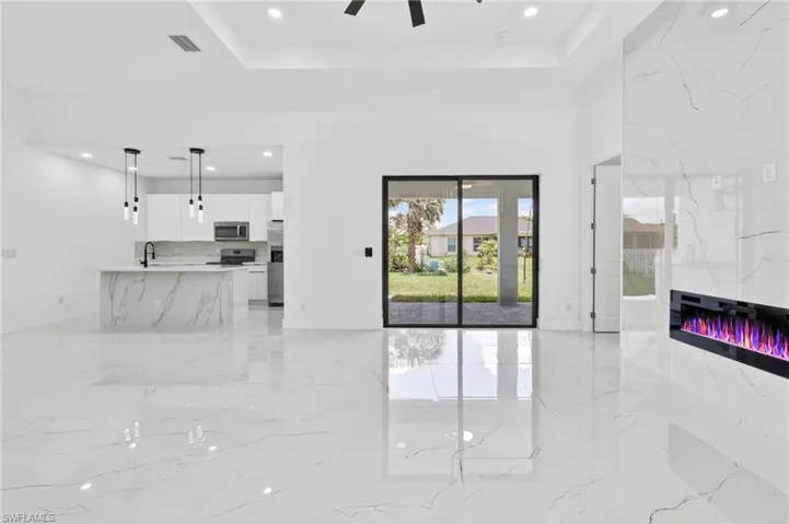 Open-concept living area featuring large format white tile flooring, a contemporary fireplace with a stone-look surround, a tray ceiling, and sliding glass doors opening to the exterior