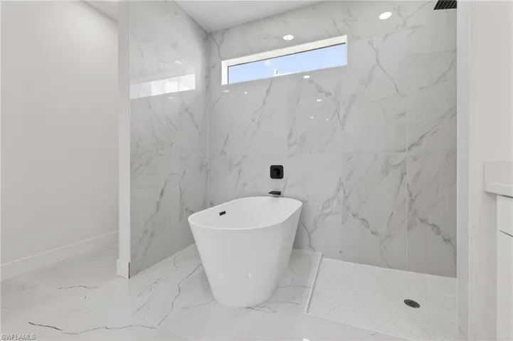 Freestanding soaking tub set against large format marbled tile walls and flooring