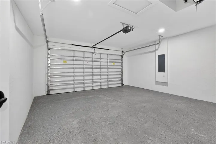 Spacious garage featuring a durable concrete floor, a sectional overhead door, an automatic opener, recessed lighting, and a visible electrical panel