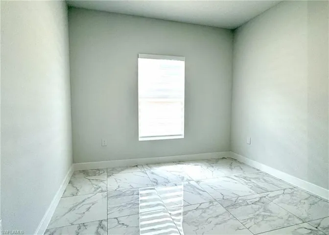 Unfurnished room featuring light marble finish flooring and baseboards