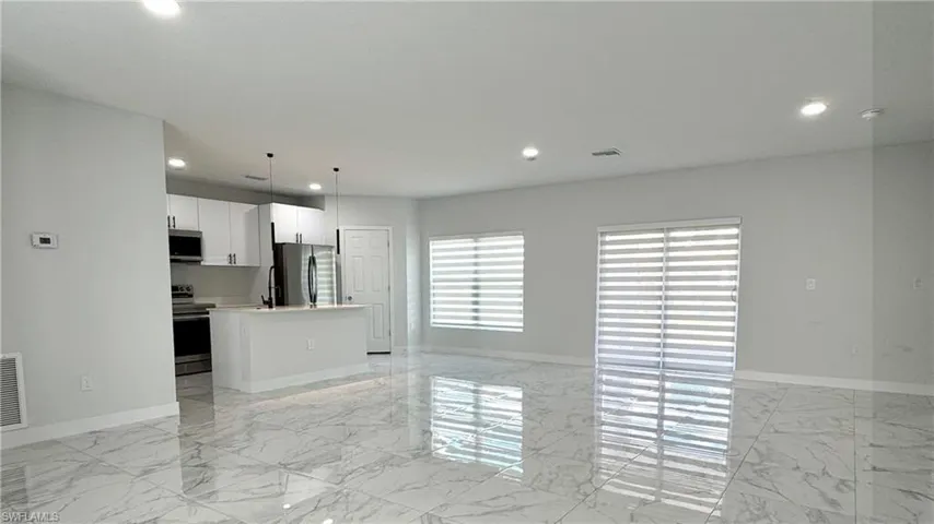 Kitchen with open floor plan, a center island, white cabinets, light marble finish floors, and stainless steel appliances