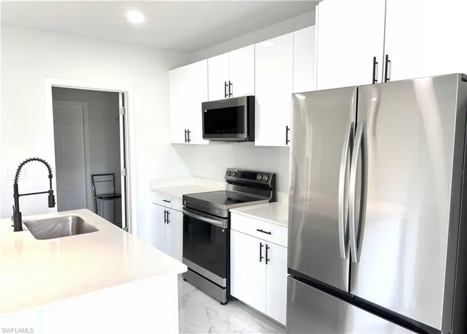 Kitchen with stainless steel appliances, light marble finish flooring, light stone countertops, white cabinets, and recessed lighting