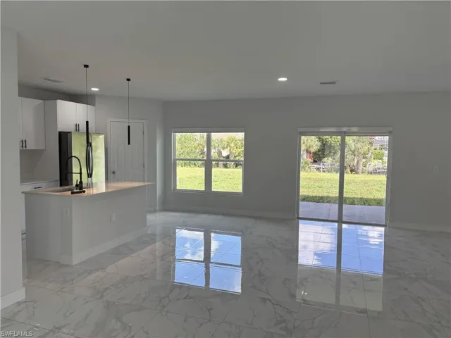 Kitchen featuring light marble finish flooring, a center island with sink, recessed lighting, freestanding refrigerator, and decorative light fixtures