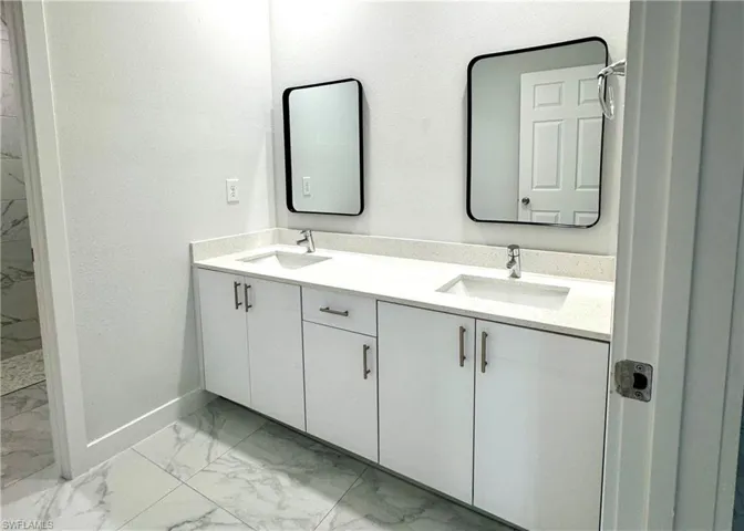 Full bath with light marble finish floors and double vanity