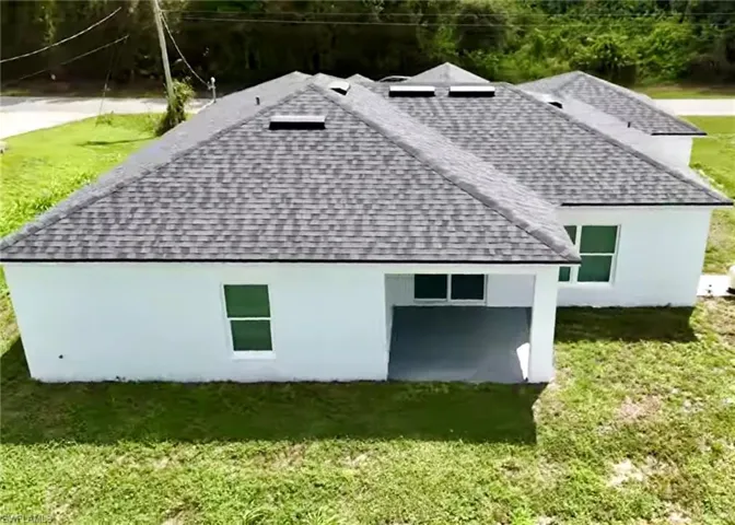 Rear view of house featuring a shingled roof and a lawn