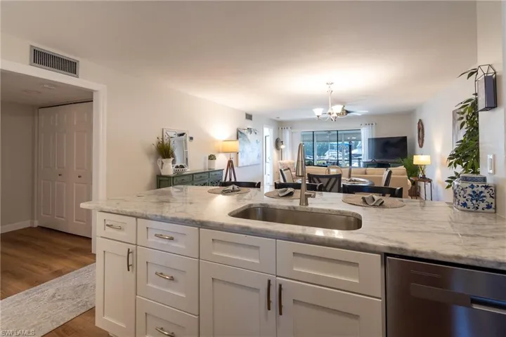 Kitchen with stainless steel dishwasher, white cabinets, light stone countertops, dark wood-type flooring, and open floor plan
