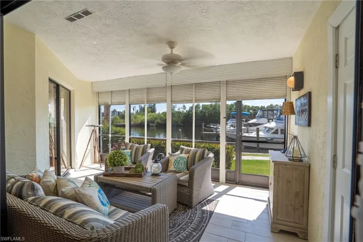 Sunroom featuring a textured wall, ceiling fan, a textured ceiling, a water view, and wood finished floors