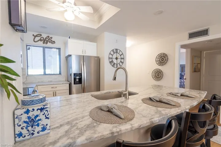 Kitchen with stainless steel refrigerator with ice dispenser, light stone countertops, a breakfast bar area, ornamental molding, and a ceiling fan