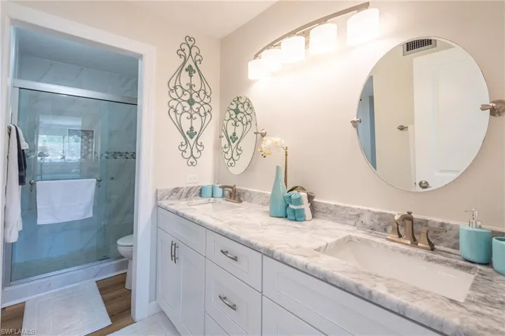 Full bathroom with a shower stall, double vanity, and light wood finished floors