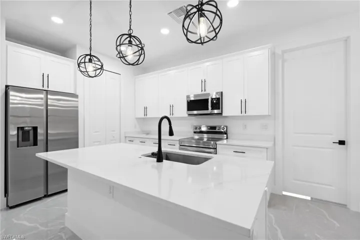 Kitchen with white cabinetry, a center island with sink, stainless steel appliances, and decorative light fixtures