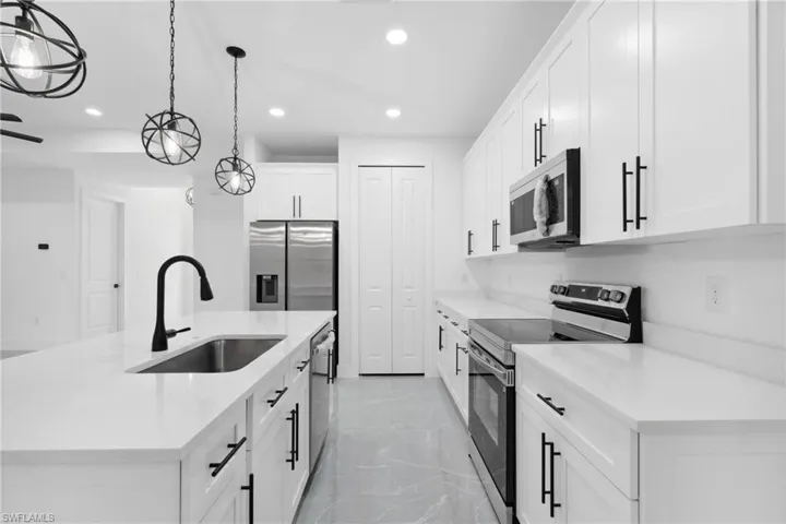 Kitchen featuring a center island with sink, sink, decorative light fixtures, white cabinetry, and stainless steel appliances