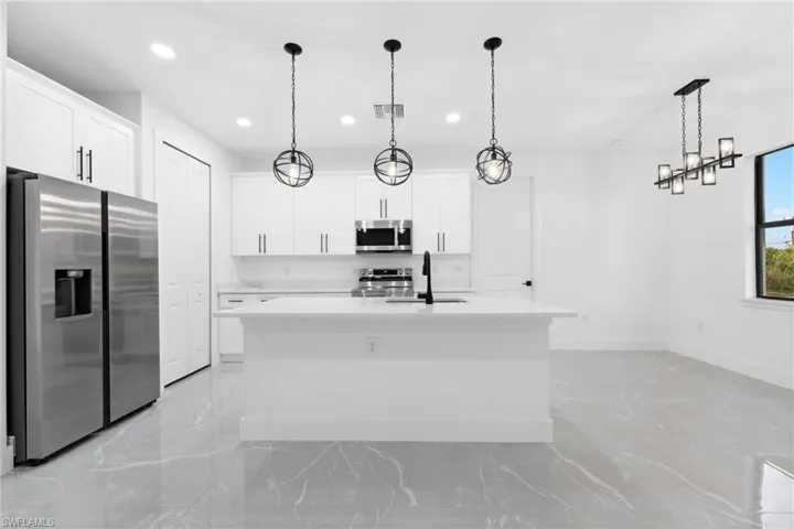Kitchen with a center island with sink, white cabinets, hanging light fixtures, and appliances with stainless steel finishes