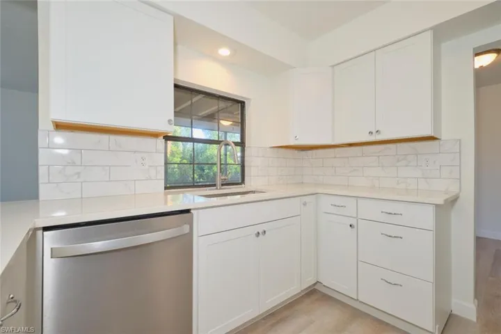 Kitchen with sink, light hardwood / wood-style flooring, stainless steel dishwasher, decorative backsplash, and white cabinetry