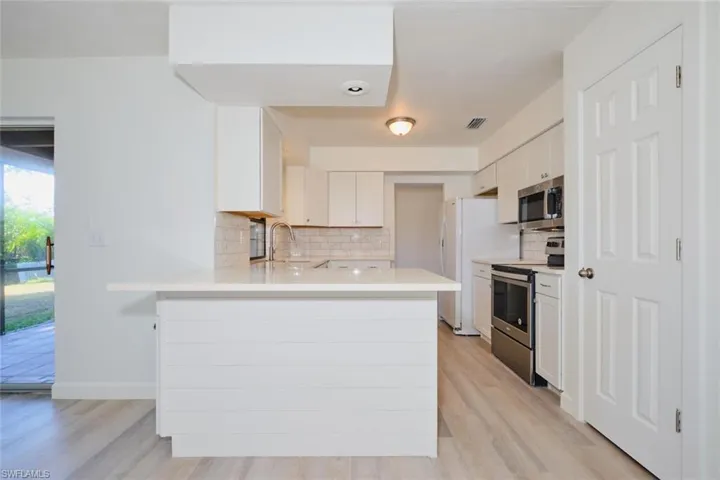 Kitchen featuring kitchen peninsula, white cabinets, light wood-type flooring, and appliances with stainless steel finishes
