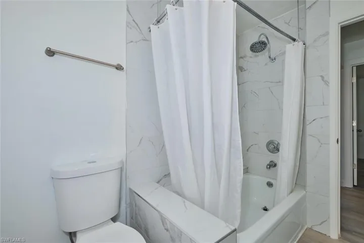 Bathroom featuring shower / bath combo, hardwood / wood-style flooring, and toilet