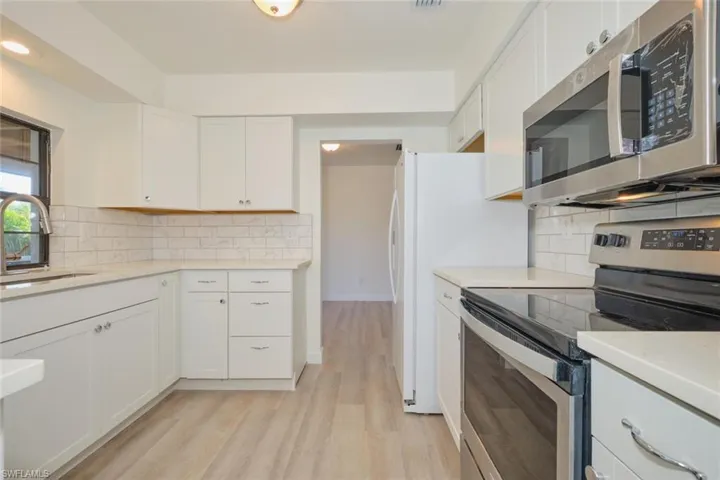 Kitchen with sink, stainless steel appliances, backsplash, white cabinets, and light wood-type flooring