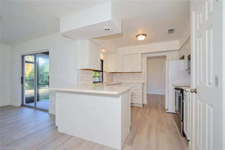 Kitchen featuring kitchen peninsula, appliances with stainless steel finishes, decorative backsplash, light hardwood / wood-style flooring, and white cabinetry