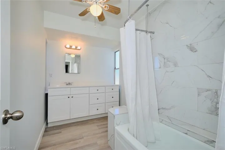 Bathroom with hardwood / wood-style flooring, vanity, ceiling fan, and shower / tub combo with curtain