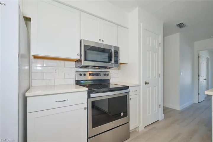 Kitchen with appliances with stainless steel finishes, backsplash, light hardwood / wood-style flooring, and white cabinetry