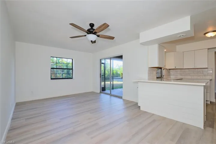 Kitchen featuring kitchen peninsula, backsplash, ceiling fan, light hardwood / wood-style floors, and white cabinetry