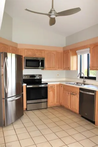 Kitchen featuring appliances with stainless steel finishes, a sink, vaulted ceiling, light countertops, and light brown cabinetry
