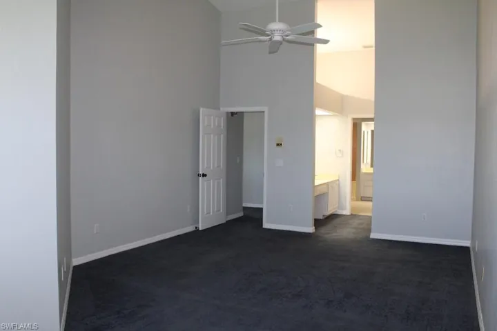 Unfurnished bedroom with high vaulted ceiling, dark colored carpet, connected bathroom, and a ceiling fan