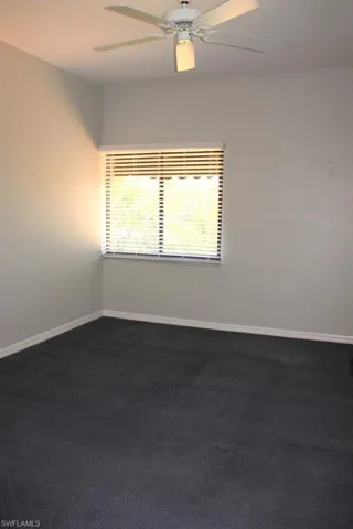 Spare room featuring a ceiling fan, dark colored carpet, and baseboards