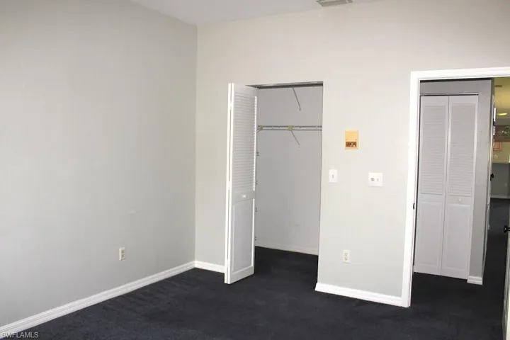 Unfurnished bedroom with dark colored carpet, baseboards, and multiple closets
