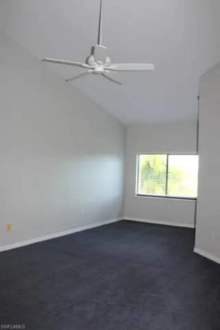 Spare room with ceiling fan, dark colored carpet, vaulted ceiling, and baseboards