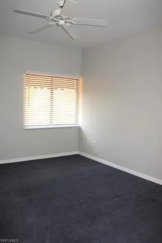 Spare room featuring a ceiling fan, dark colored carpet, and baseboards