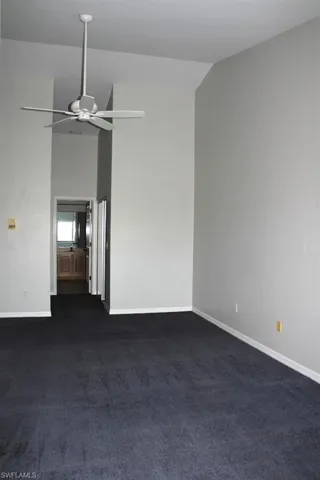 Unfurnished room with a ceiling fan, vaulted ceiling, baseboards, and dark carpet