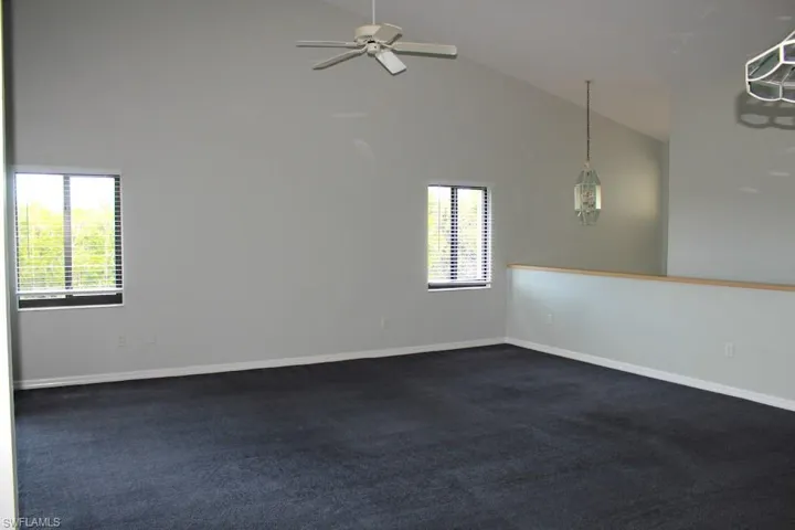Spare room with high vaulted ceiling, a ceiling fan, dark colored carpet, and baseboards