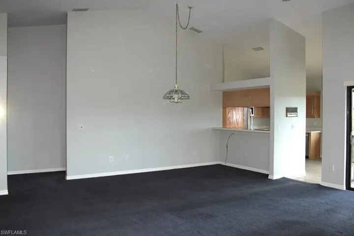 Unfurnished living room featuring dark colored carpet, baseboards, and high vaulted ceiling