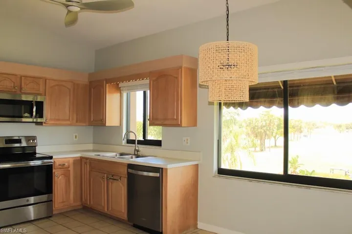 Kitchen with stainless steel appliances, a sink, vaulted ceiling, a chandelier, and light countertops